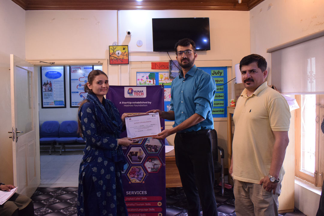 A student receives a certificate from an instructor during the certificate distribution ceremony of the Digital Marketing and SEO course at Hunar Tech Rawalpindi, with a banner in the background showing the Hunar Tech logo and mission.