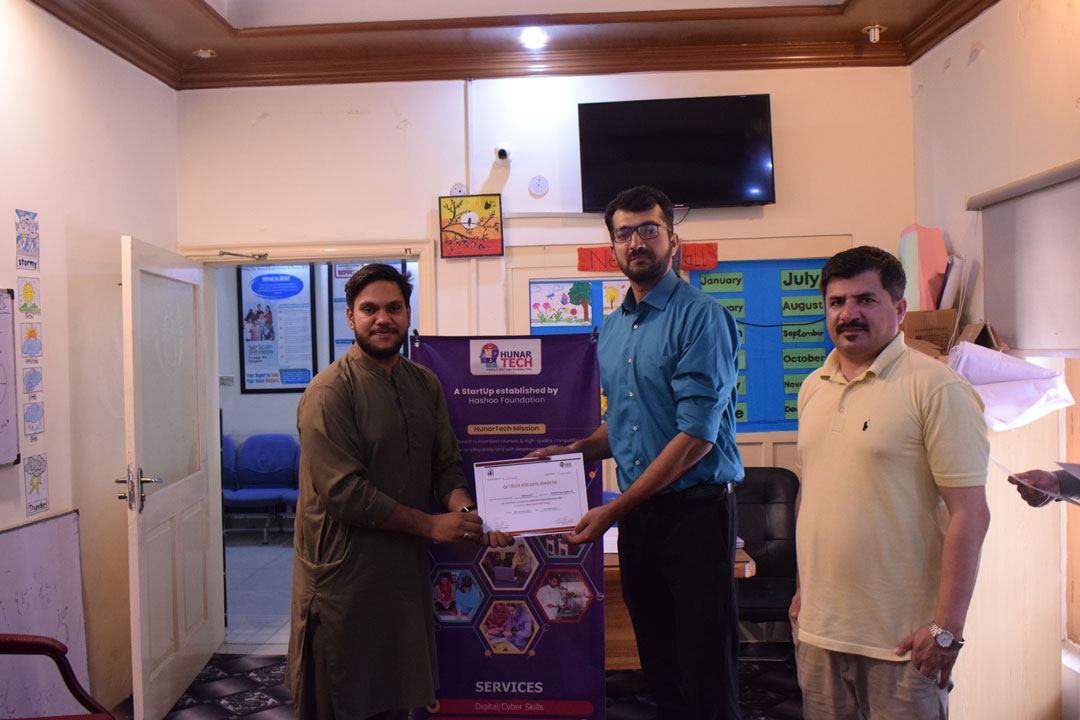 A student receives a certificate from an instructor during the certificate distribution ceremony of the Digital Marketing and SEO course at Hunar Tech Rawalpindi, with a banner in the background showing the Hunar Tech logo